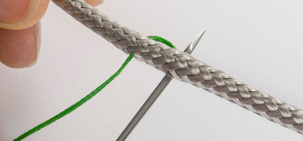 Stitching a splice on a grey rope with a needle and green thread